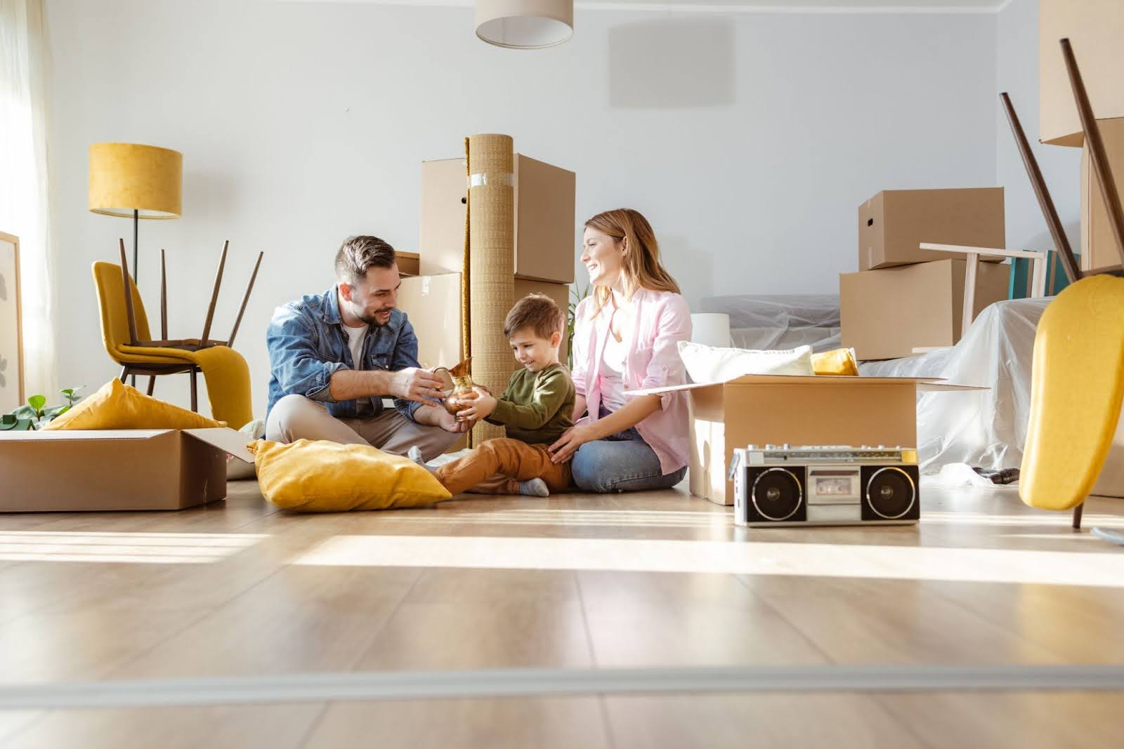 Parents and their child sitting on a lounge room floor, surrounded by boxes